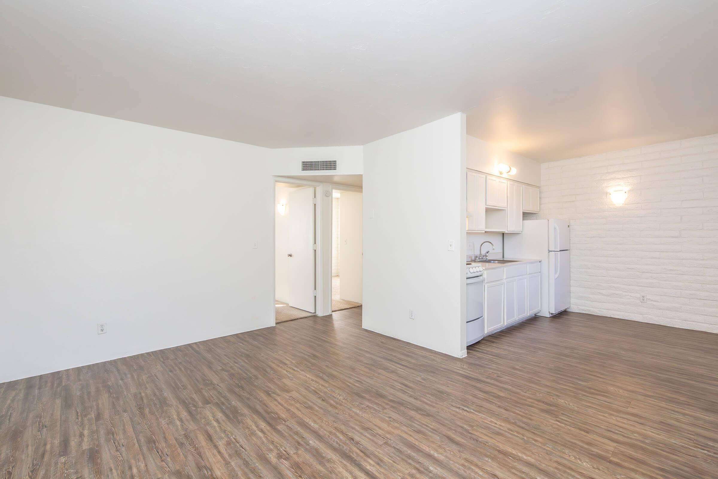 Bright and airy living space featuring modern hardwood floors, an open corner kitchen with white cabinetry, and a minimalist design.