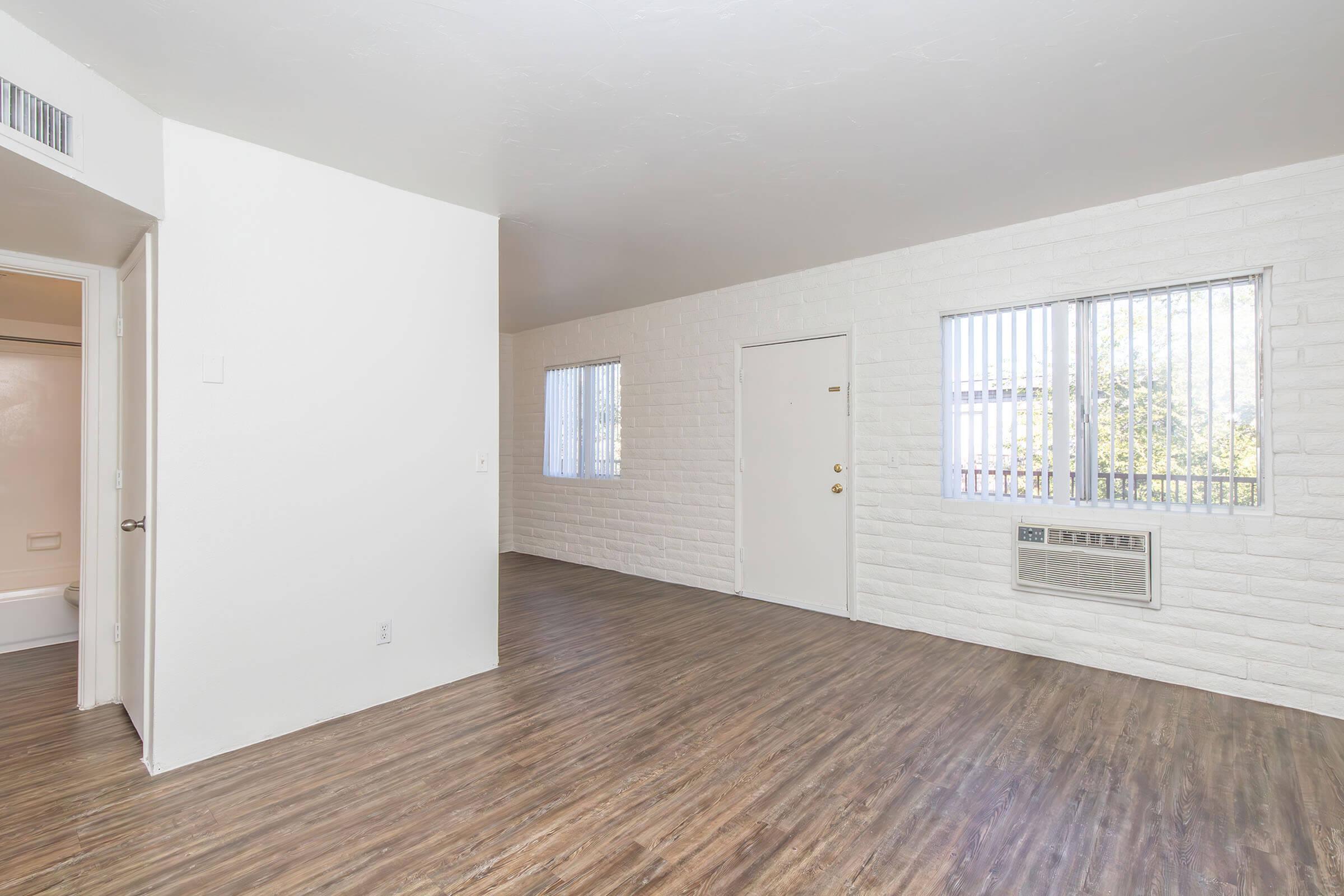 Bright, airy living space with elegant wood flooring, large windows, and stylish exposed brick walls.