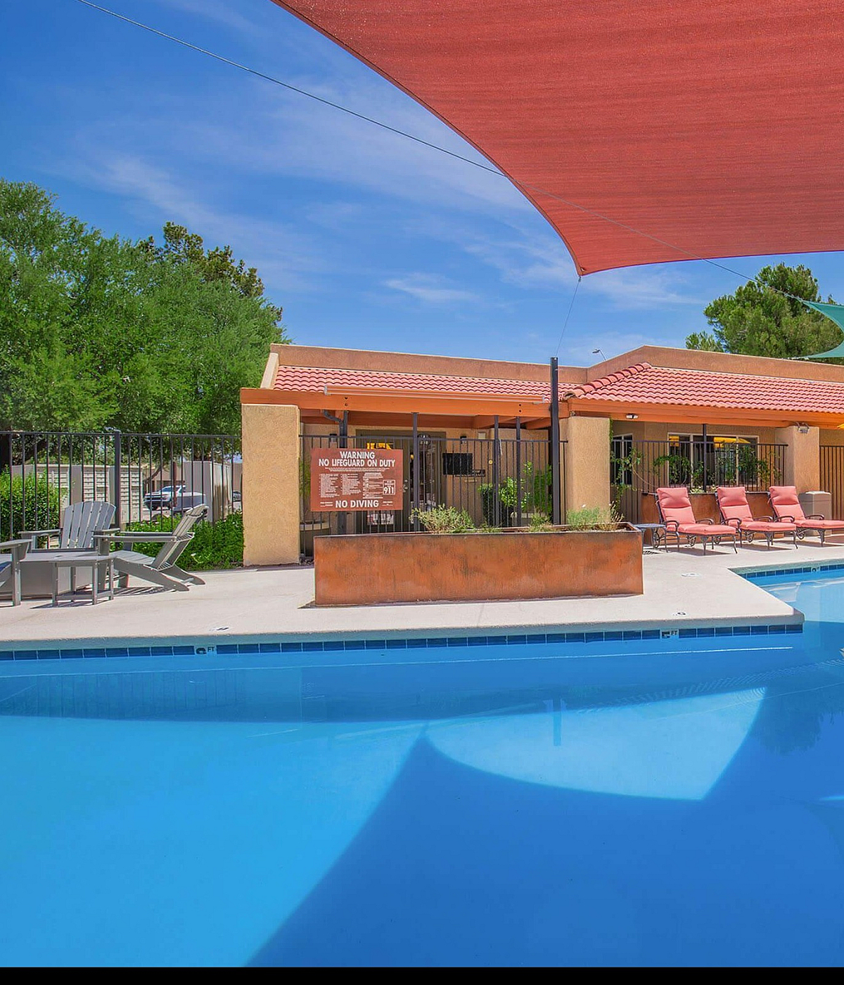 Inviting outdoor pool area with vibrant sunshades, lounge seating, and tables with umbrellas in a serene apartment community setting.