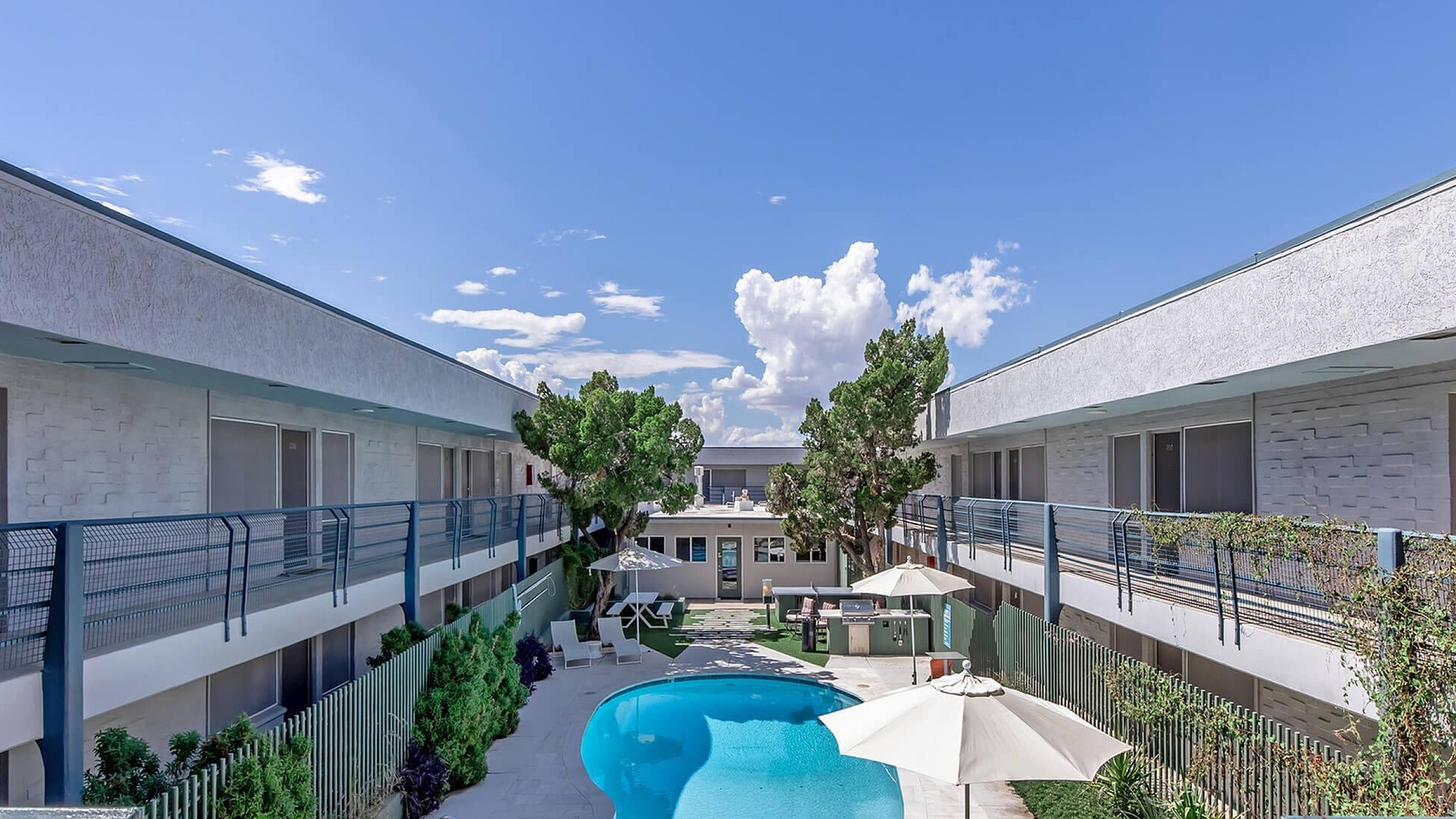 Charming apartment complex showcasing a spacious central courtyard with a sparkling pool, shaded seating, and lush greenery.