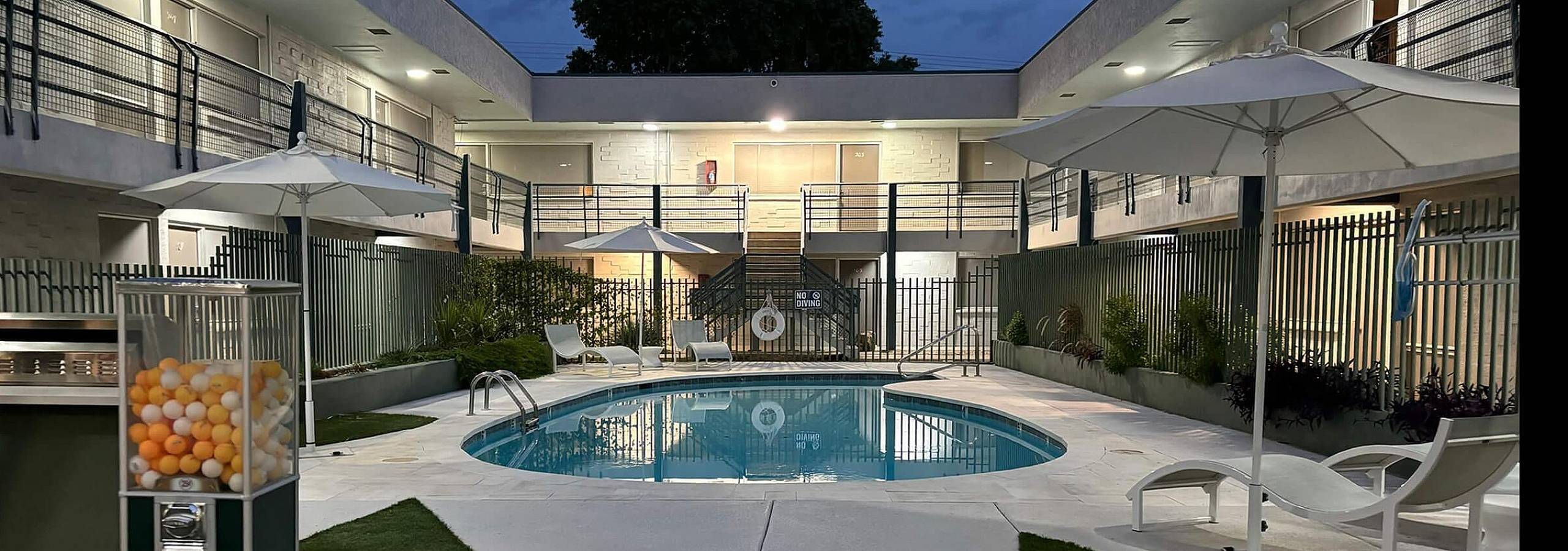 Elegant apartment complex featuring a serene courtyard with a sparkling pool, stylish loungers, and modern architecture under evening skies.