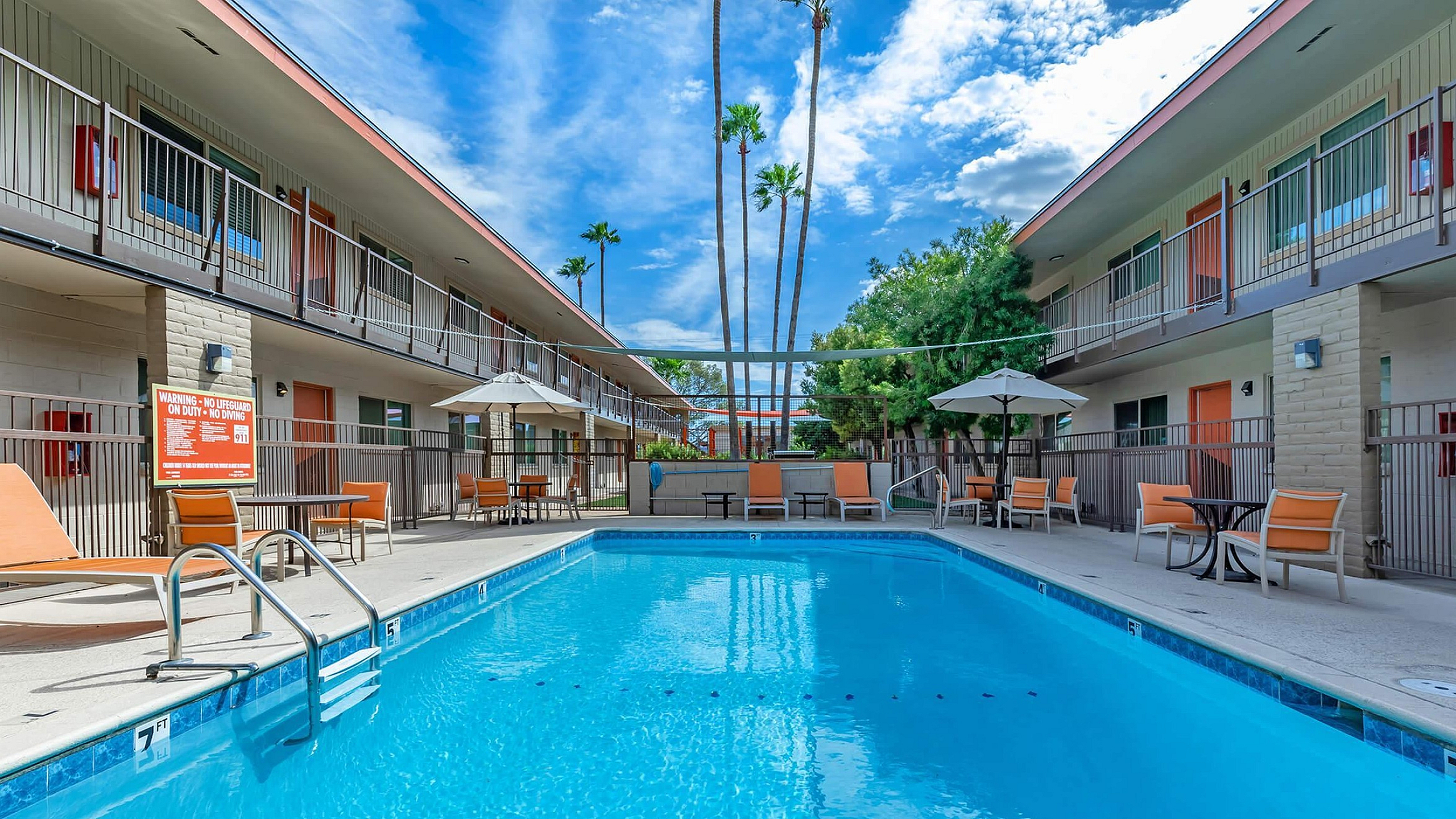 Inviting courtyard view featuring a sparkling swimming pool, surrounded by comfortable lounge chairs and modern patio umbrellas in a vibrant apartment complex.
