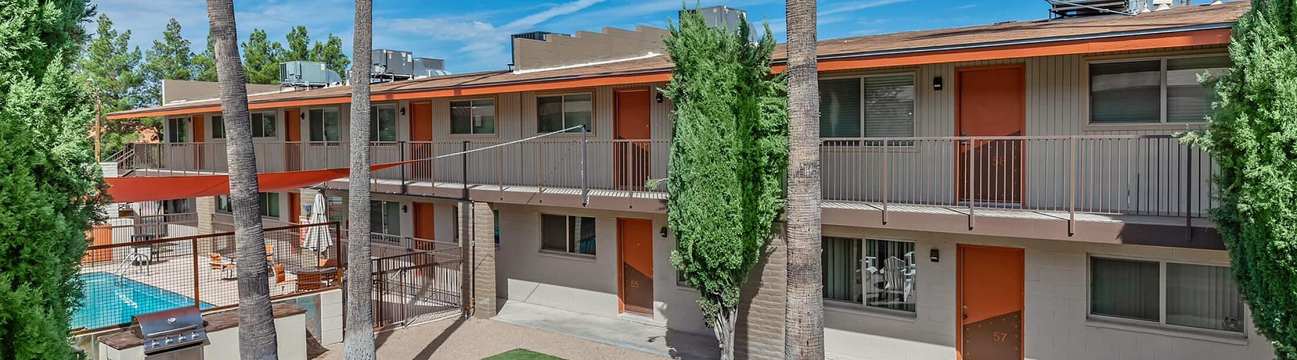 Vibrant apartment complex with lush greenery, a central fire pit, and inviting outdoor seating, offering modern amenities and a refreshing pool view.