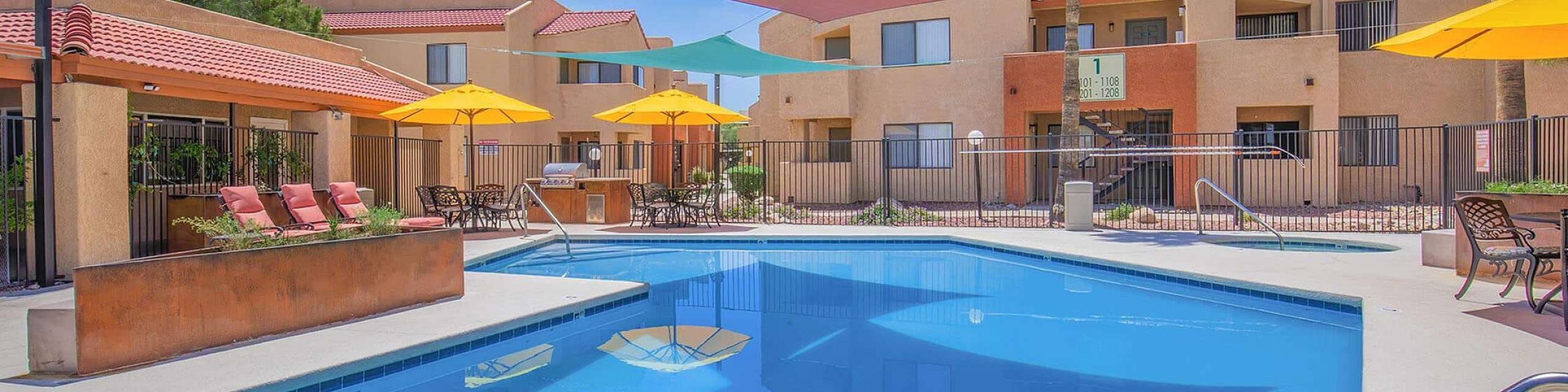 Beautiful apartment complex with a shimmering pool, vibrant sunshades, and inviting lounge area, perfect for relaxation and summer enjoyment.