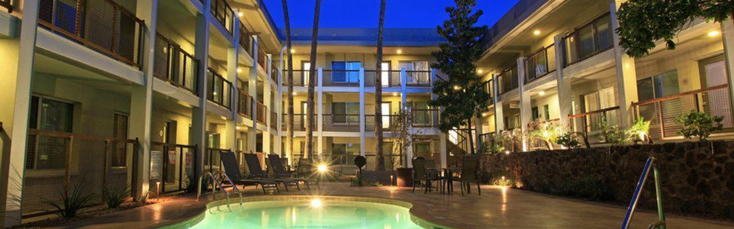 Elegant apartment complex illuminated at night featuring a serene swimming pool surrounded by lush greenery and cozy seating areas.
