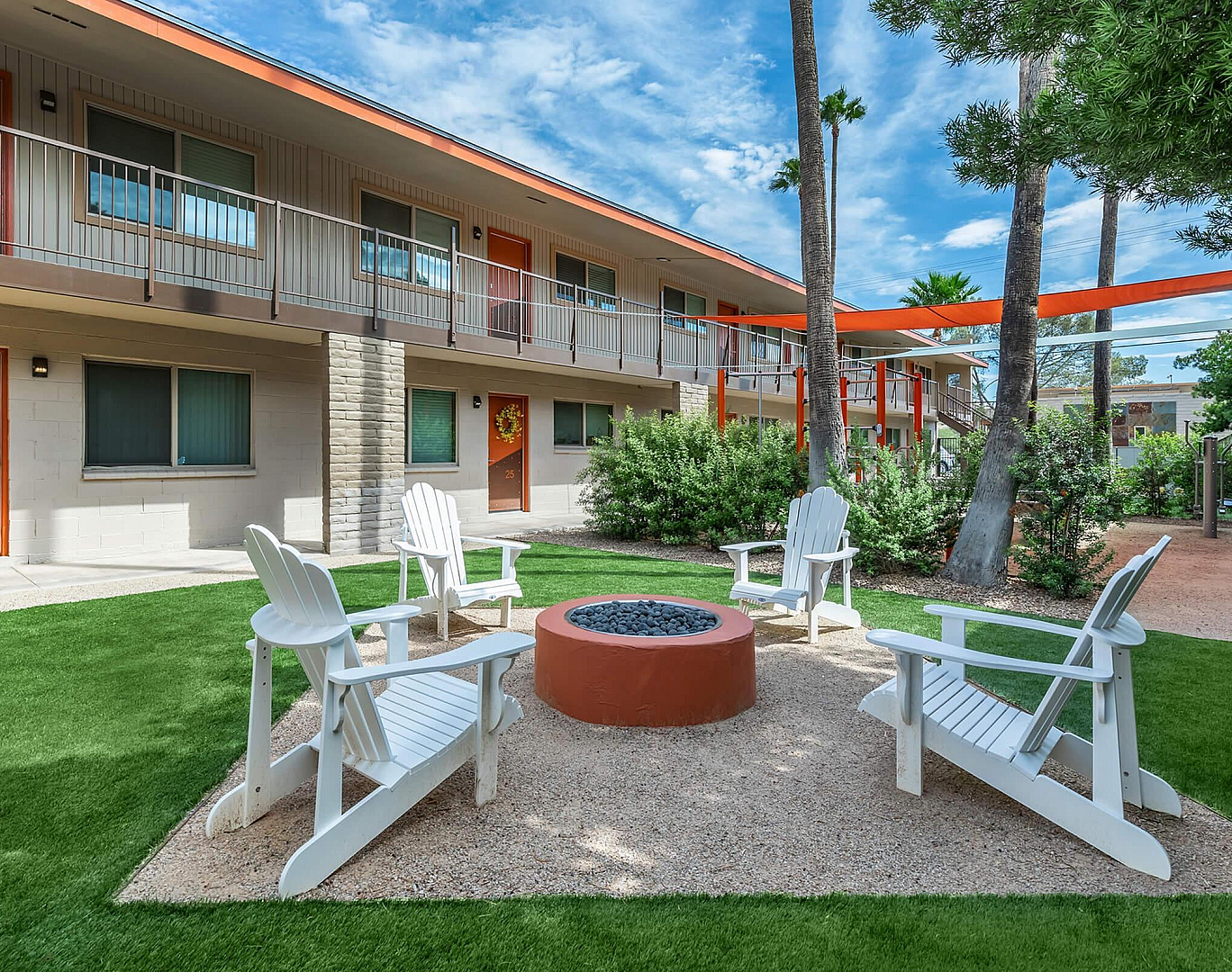 Charming outdoor courtyard with a cozy fire pit surrounded by Adirondack chairs and lush greenery, ideal for relaxation in this vibrant apartment community.