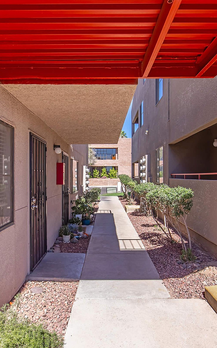Charming apartment entrance featuring a vibrant red awning, cozy walkway, and well-maintained landscaping.