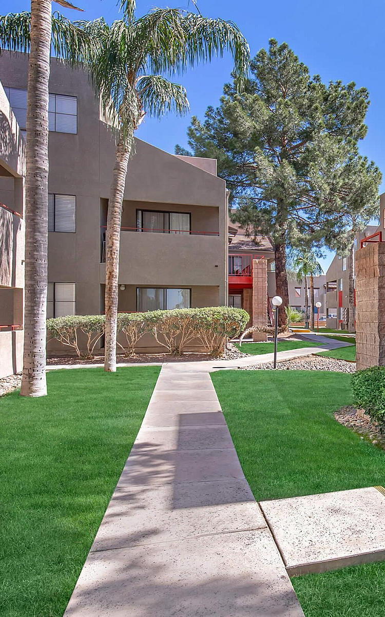 Charming apartment complex with modern architecture, lush green lawns, and inviting outdoor pathways surrounded by palm trees.
