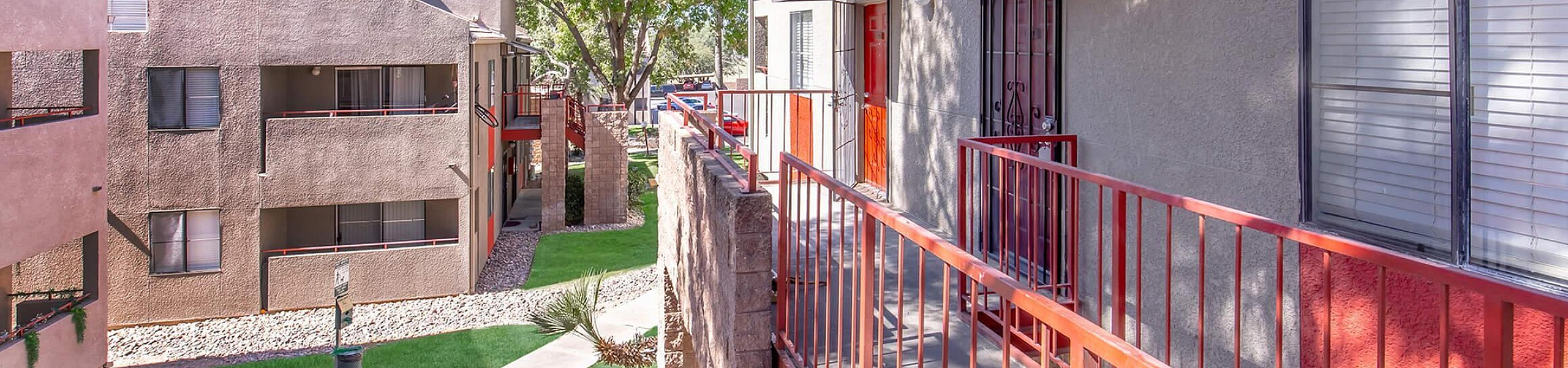 Charming apartment complex with vibrant red accents, surrounded by lush greenery and well-maintained pathways.