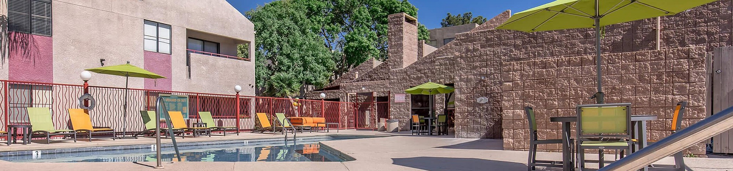 Bright, modern apartment courtyard with inviting pool, sun loungers, and shaded seating, perfect for relaxation and social gatherings.