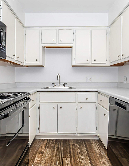 Elegant kitchen with sleek black appliances, ample white cabinetry, and warm wood flooring, perfect for modern living.