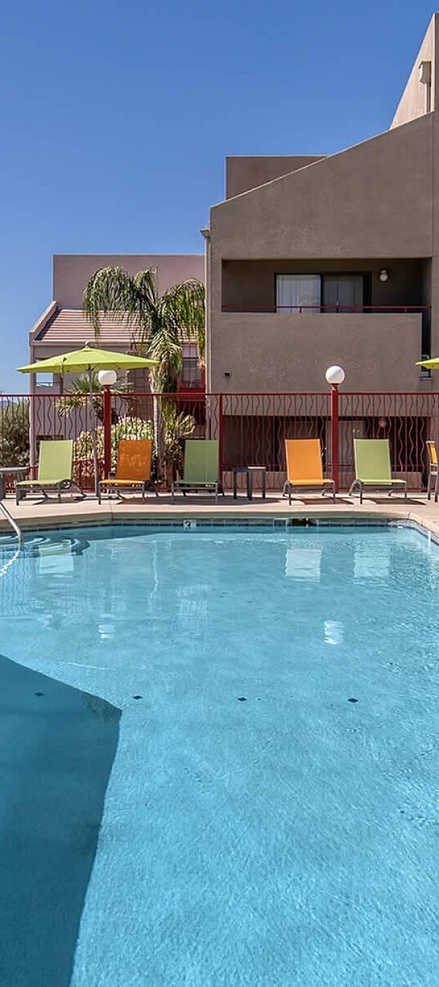 Inviting apartment complex with a refreshing swimming pool, surrounded by modern architecture and vibrant sun loungers under clear skies.