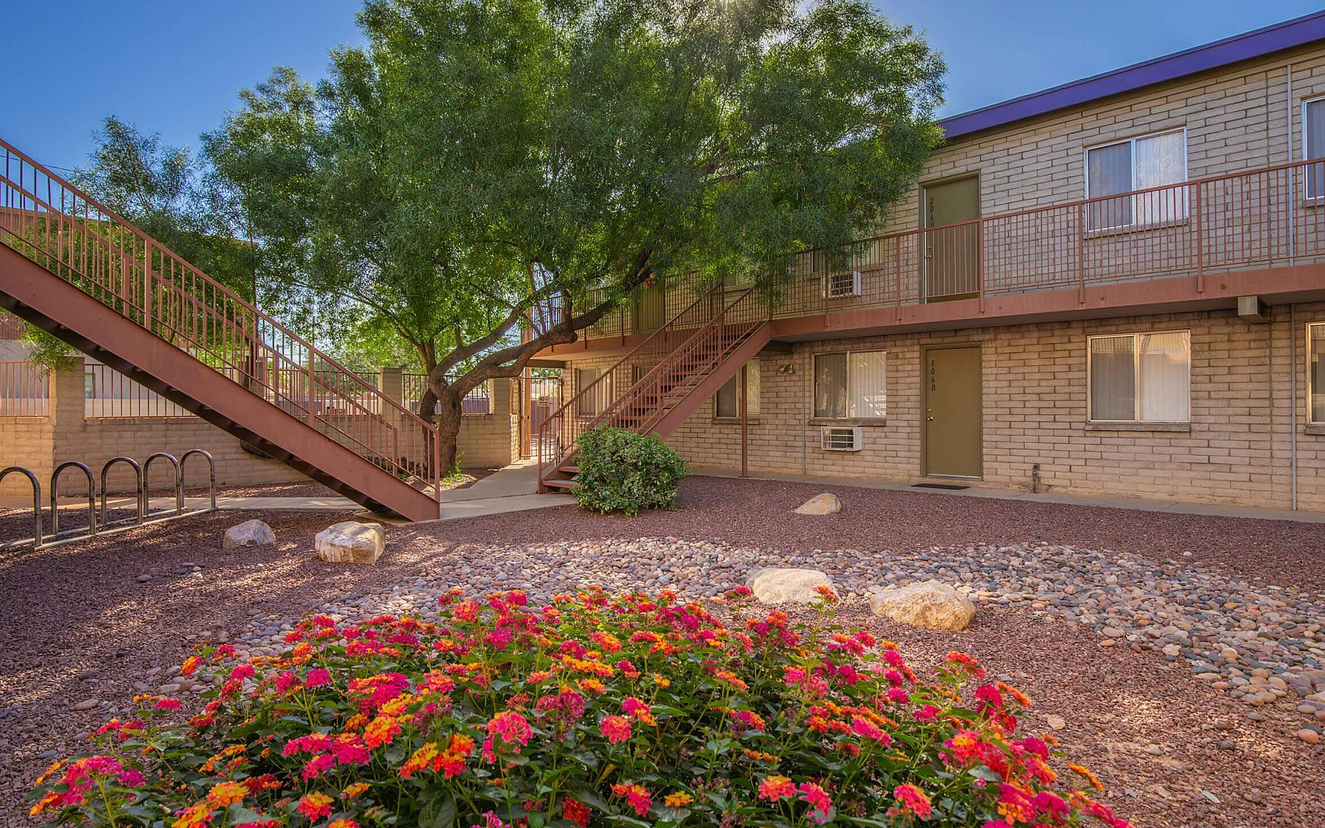 Charming apartment exterior with a lush tree and vibrant flower garden, offering serene views and inviting atmosphere.