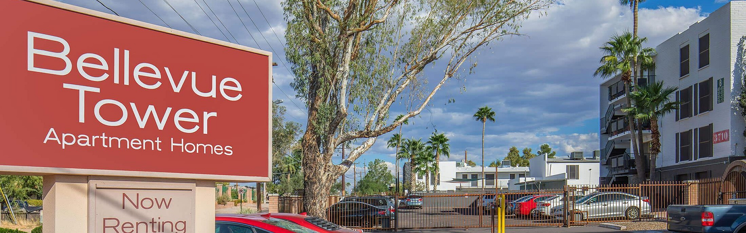 Bellevue Tower Apartment Homes entrance with vibrant sign, available for rent, set in a sunny, palm-lined neighborhood.