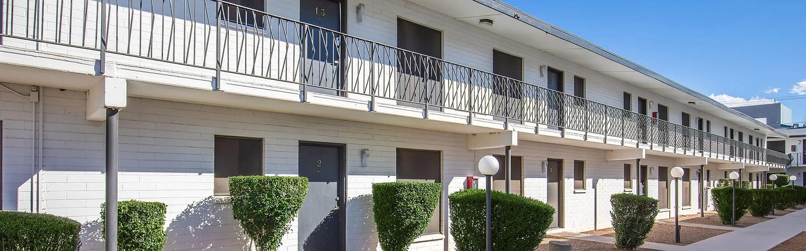 Charming apartment complex with modern exterior, featuring neatly trimmed shrubs and a spacious walkway.