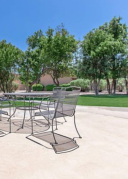 Charming outdoor patio area with modern seating overlooking lush greenery and a bright blue sky.