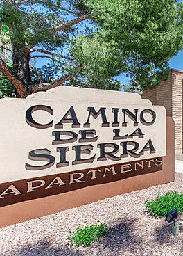 Inviting exterior view of Camino De La Sierra Apartments with lush greenery and charming brick architecture.