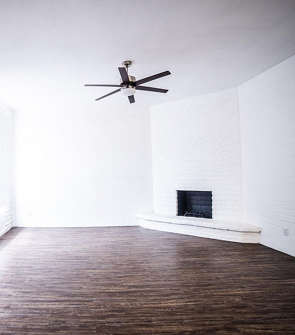 Bright and spacious living room with elegant hardwood floors, featuring a sleek ceiling fan and a cozy white brick fireplace.