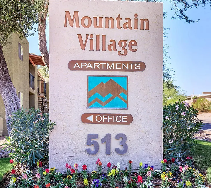 Inviting entrance sign for Mountain Village Apartments surrounded by lush greenery and colorful flowers, highlighting a serene living environment.