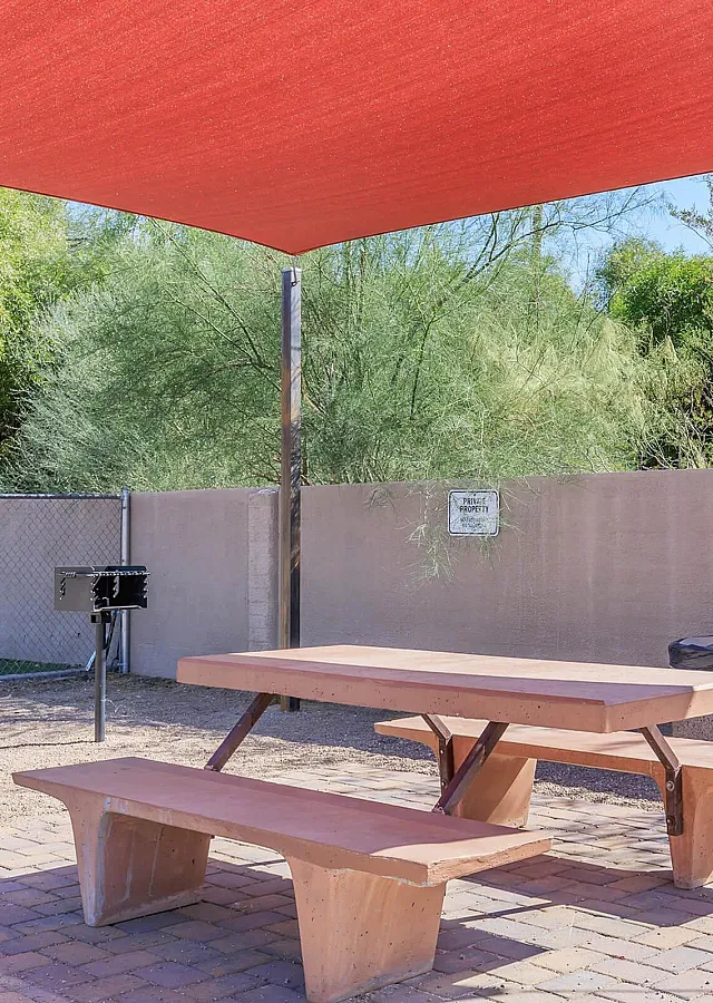 Charming outdoor picnic area with a wooden table set under a vibrant red sunshade, ideal for relaxing gatherings.