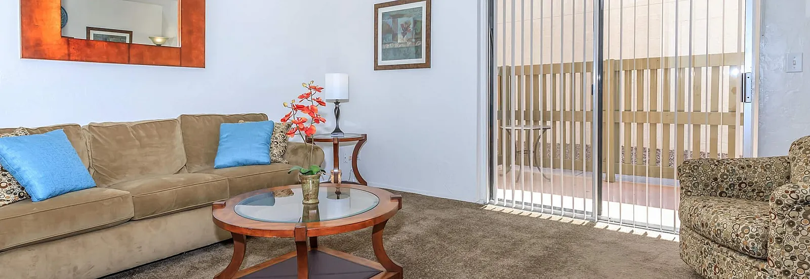 Inviting living room with plush beige sofa, vibrant orange wall mirror, and floor-to-ceiling window offering ample natural light.