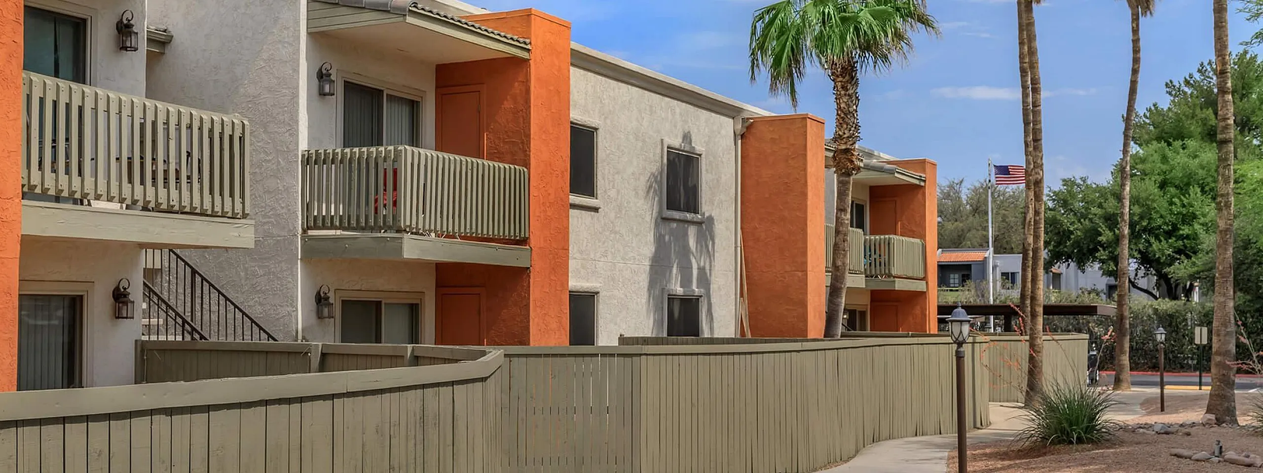 Charming apartment complex with vibrant orange and cream exteriors, featuring private balconies, palm trees, and a well-maintained walkway.