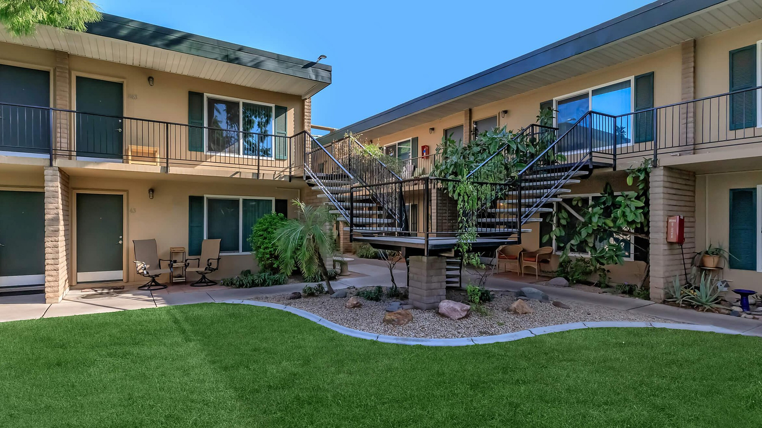Charming courtyard view of a modern apartment complex with lush greenery, inviting seating areas, and sleek architectural features.