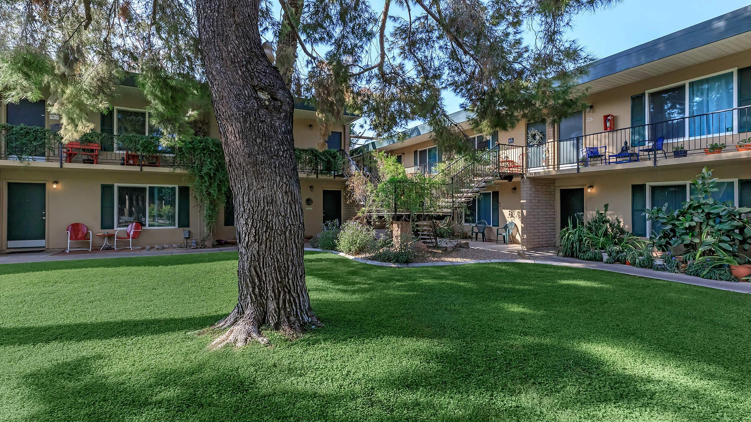 Charming apartment complex with verdant lawn, mature trees, and inviting balconies, ideal for relaxed living.