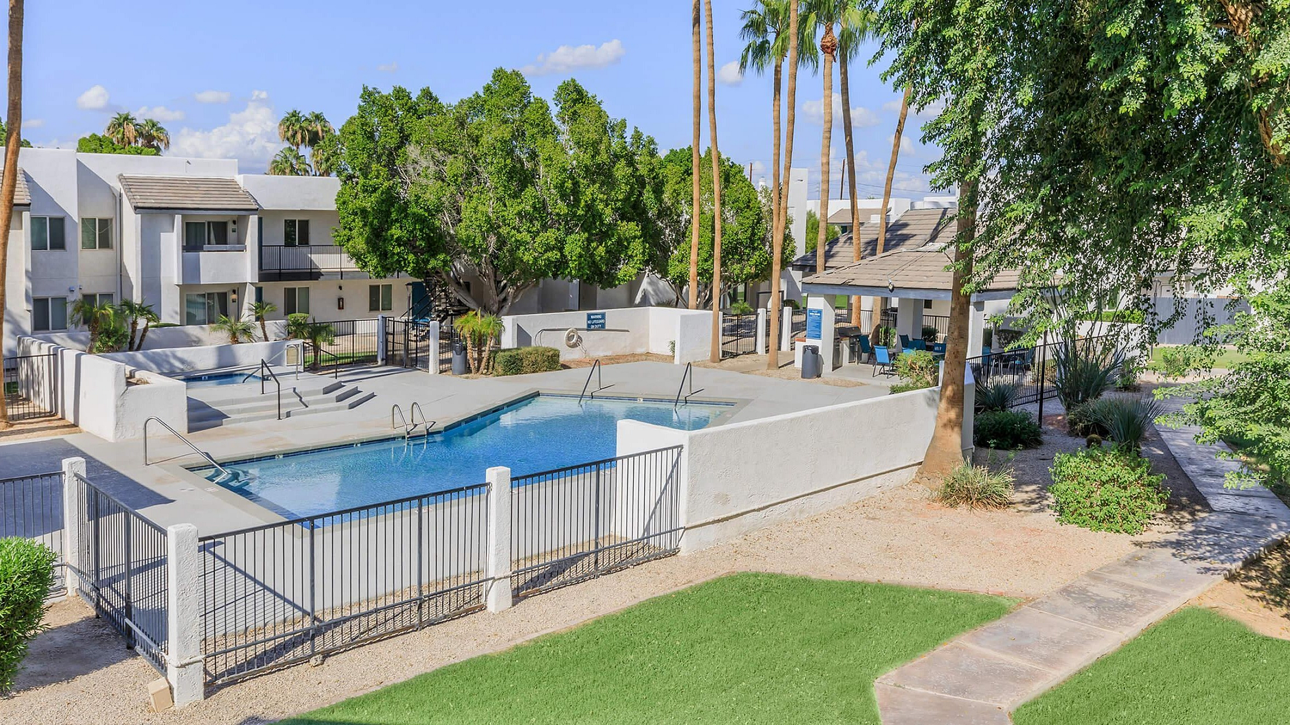 Inviting apartment complex featuring a glistening outdoor pool surrounded by lush greenery and palm trees, offering a slice of paradise.