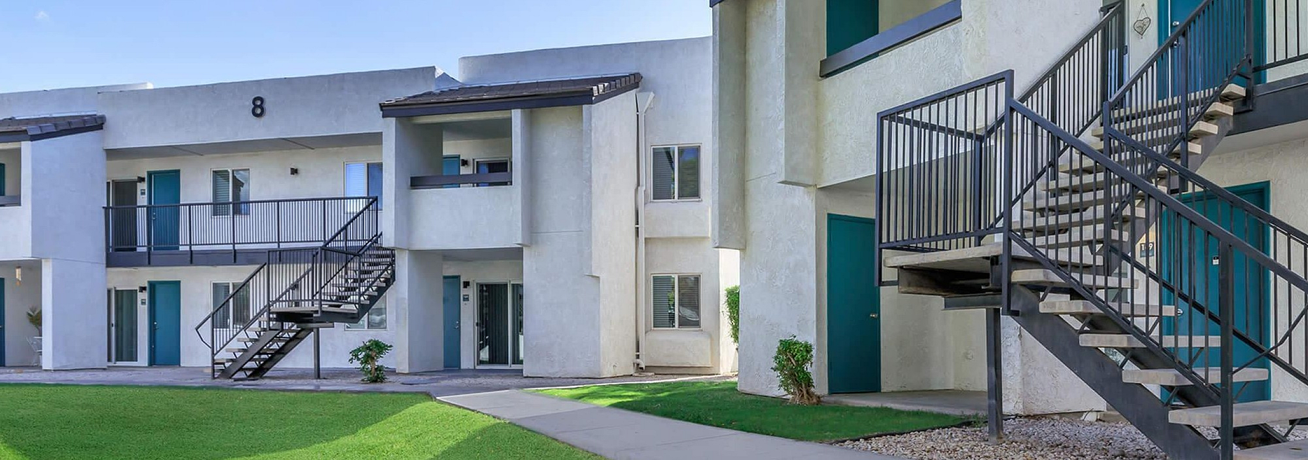 Modern apartment complex with lush greenery, featuring outdoor staircases and spacious balconies.