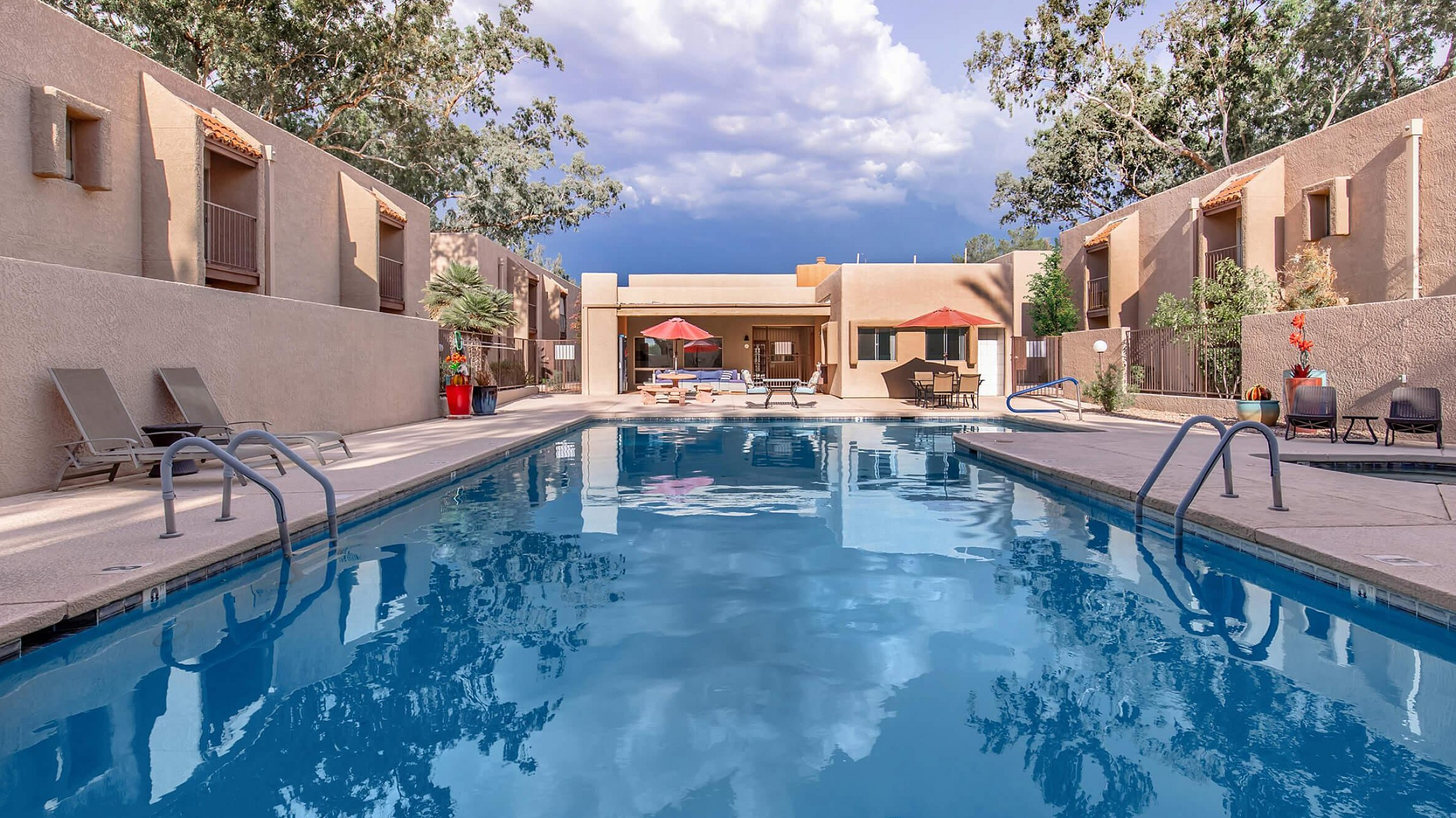 Inviting outdoor swimming pool with modern lounge chairs and umbrellas, surrounded by stylish apartment buildings and lush greenery.