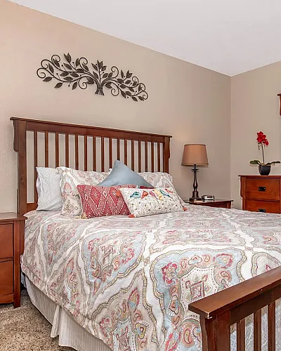 Elegant bedroom featuring a wooden bed frame, cozy patterned bedding, and stylish decor, creating a warm and inviting atmosphere.