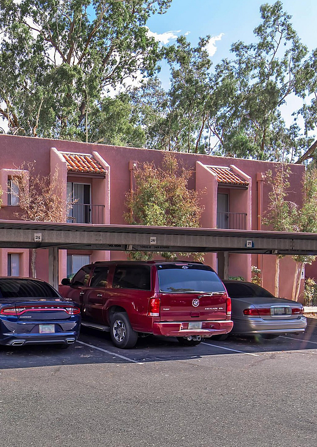 Charming apartment building with vibrant facade surrounded by lush greenery and convenient covered parking.