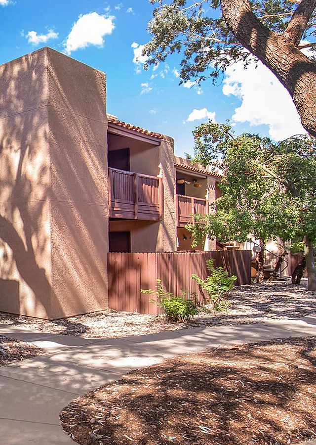 Charming desert-style apartment building with wooden balconies and beautiful mature trees casting artistic shadows.