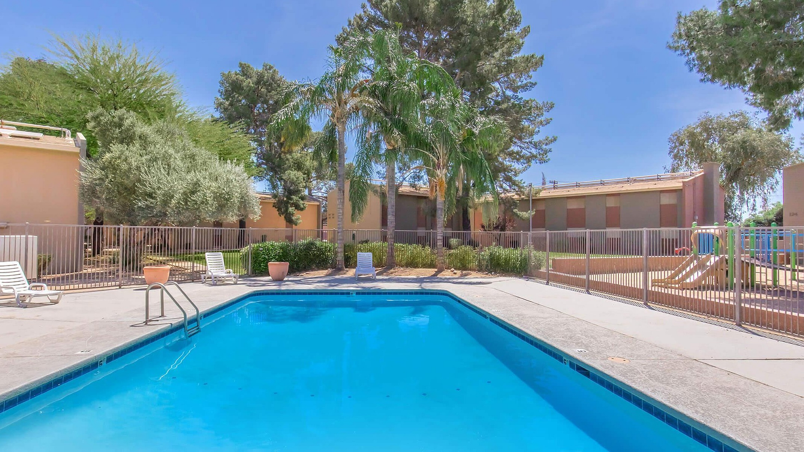Inviting apartment community pool surrounded by lush greenery and relaxing lounge chairs, perfect for enjoying sun-filled days.
