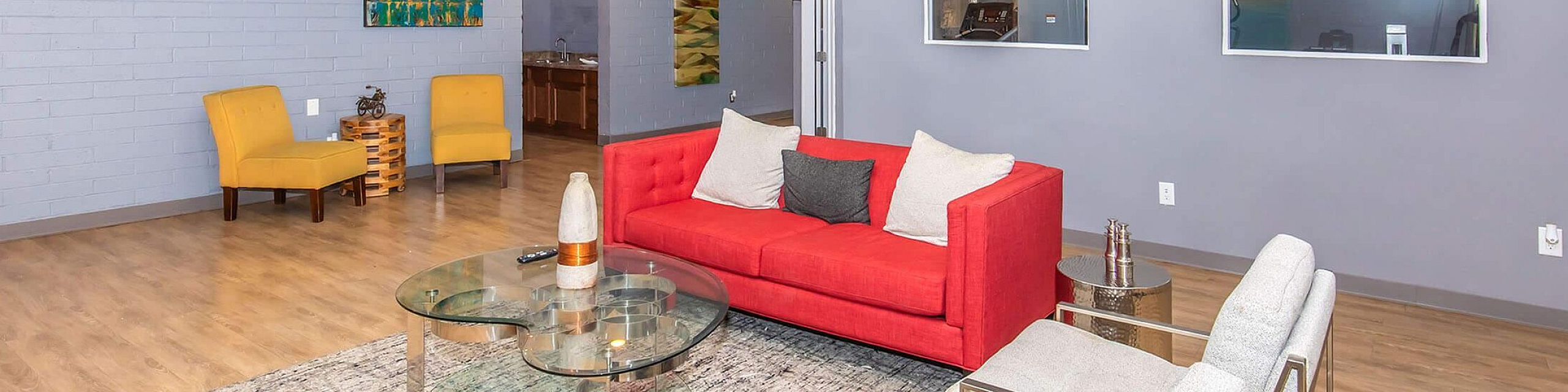 Modern living room with a vibrant red sofa, elegant glass coffee table, and sleek decor featuring colorful art on the wall.
