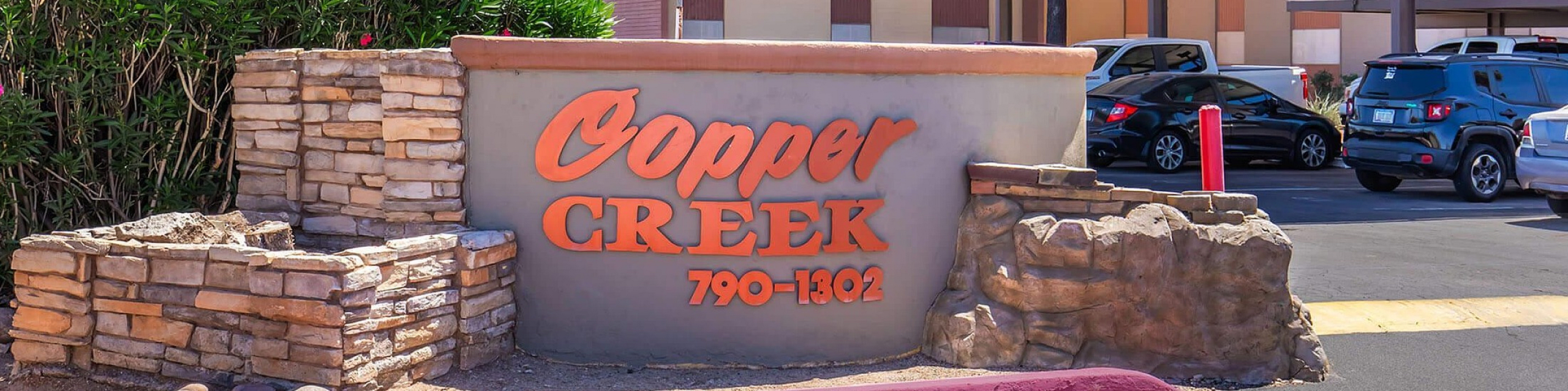 Charming entrance to Cooper Creek apartments with lush greenery and ample parking.