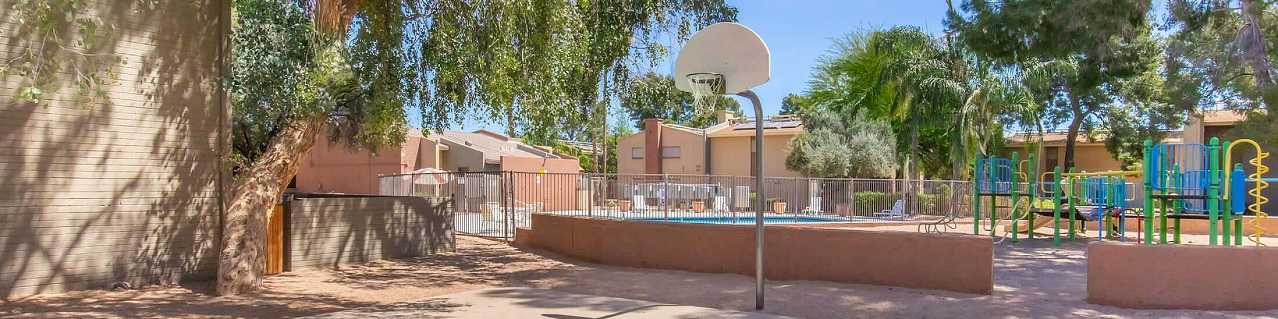 Sunny outdoor basketball court and vibrant playground area surrounded by lush trees, ideal for family activities.