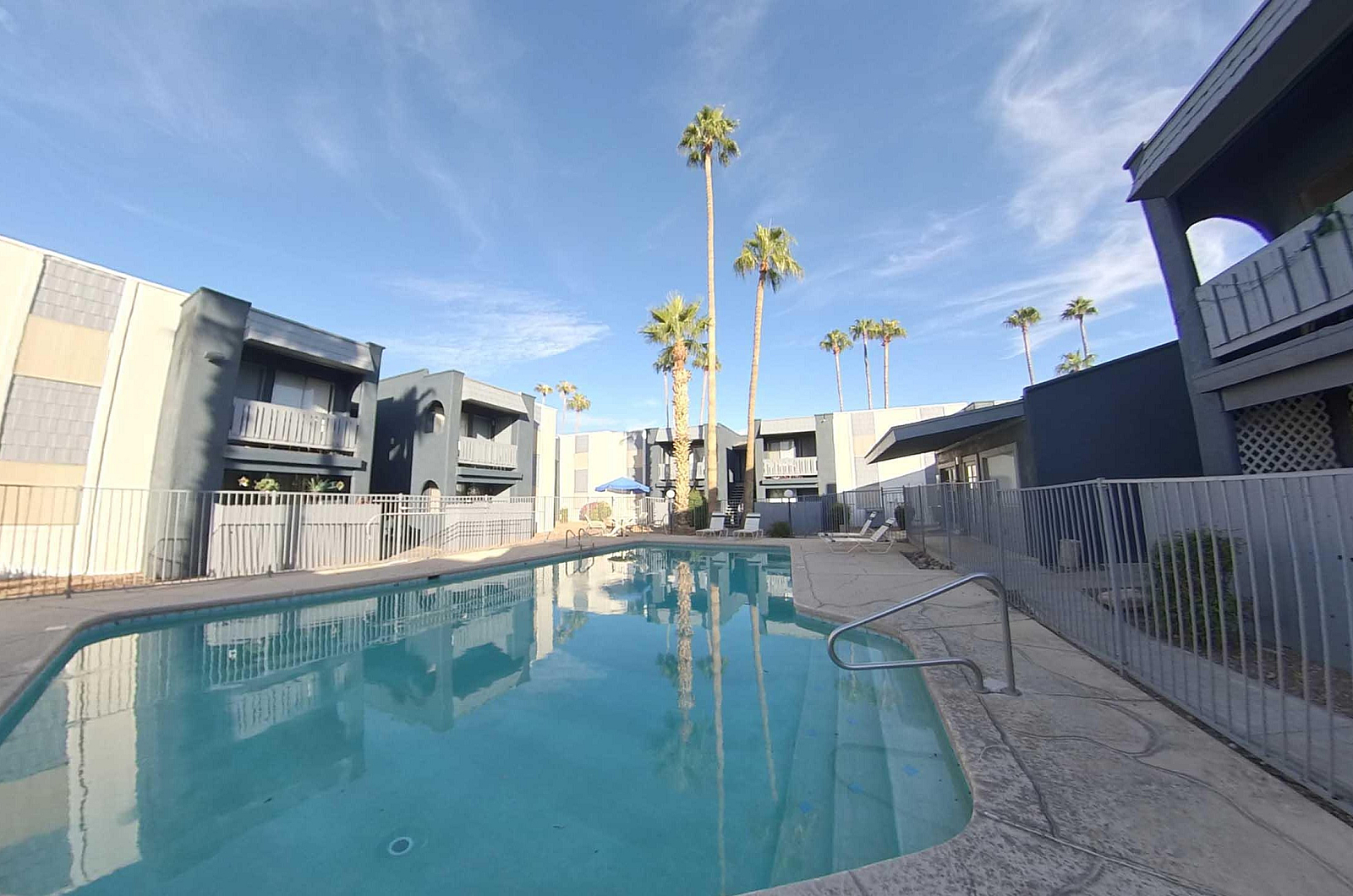 Charming apartment complex featuring a sunlit pool surrounded by lush palm trees, perfect for relaxation and enjoying the serene outdoor atmosphere.