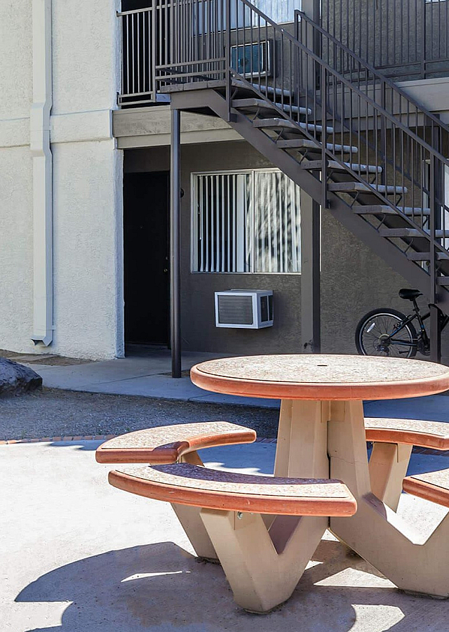 Charming apartment exterior with a cozy courtyard featuring a round picnic table, nestled under palm trees and near modern staircases.