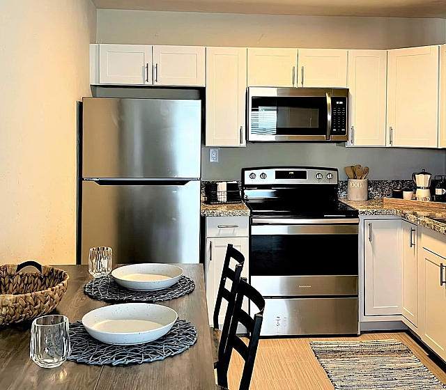 Chic apartment kitchen with modern appliances, white cabinetry, and cozy dining setup for intimate meals.