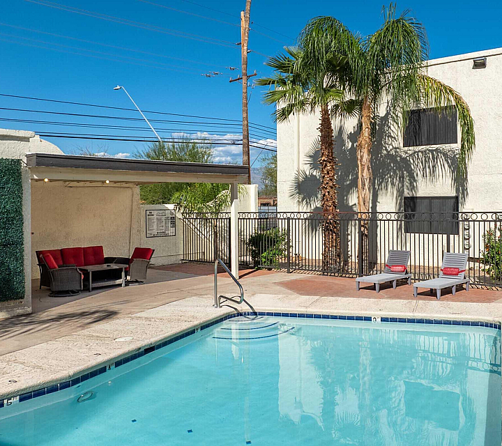 Inviting outdoor pool area with modern lounge chairs, vibrant red seating, and lush palm trees under a clear blue sky.