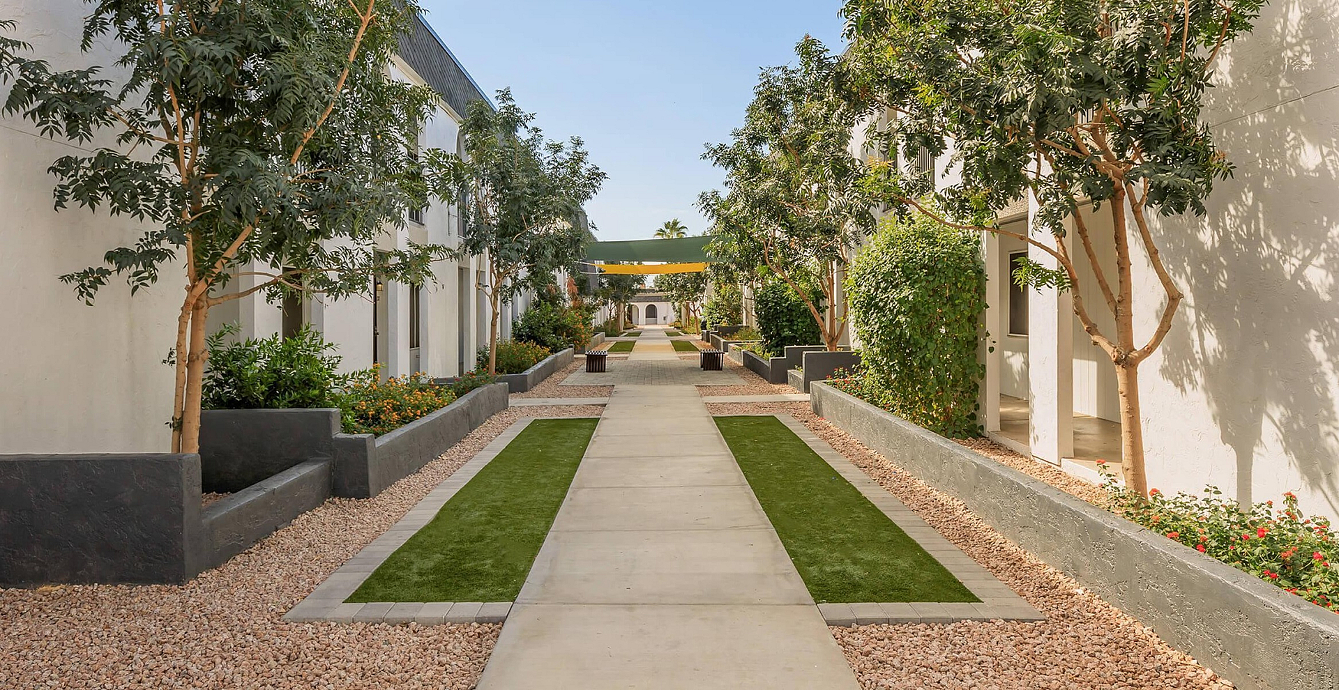 Serene apartment walkway lined with lush greenery and elegant landscaping, offering a peaceful and inviting entrance.