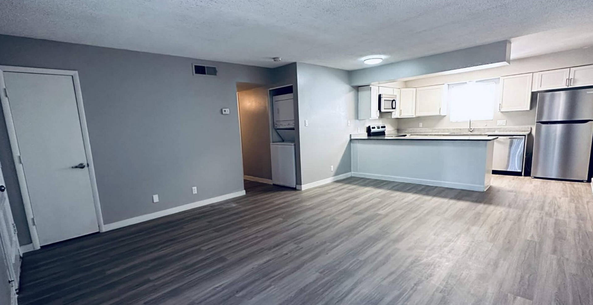Spacious open-plan living area with sleek hardwood floors, modern kitchen featuring stainless steel appliances, and ample natural light.