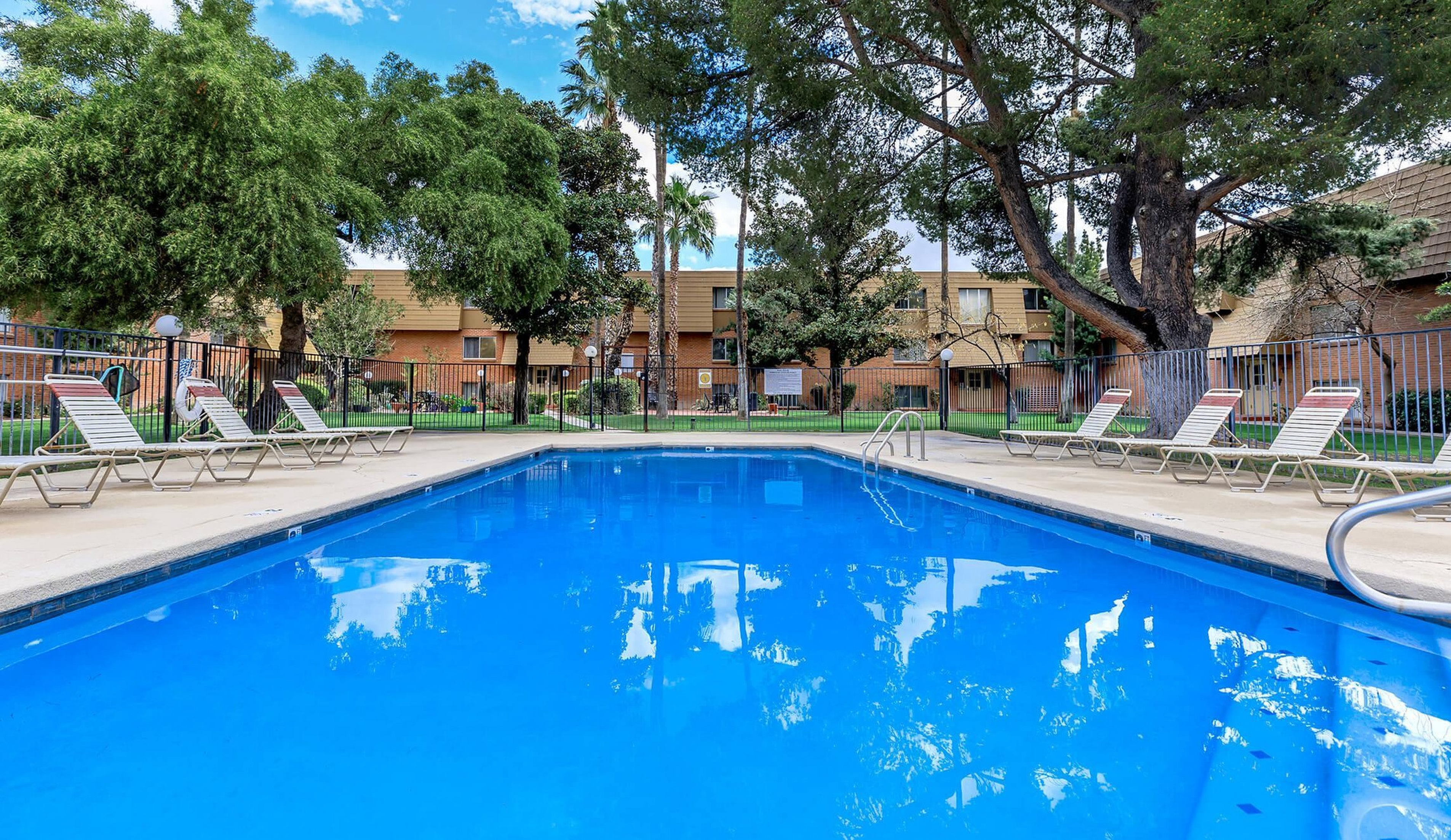Inviting outdoor pool surrounded by lush greenery and cozy lounge chairs, perfect for relaxation and leisure.