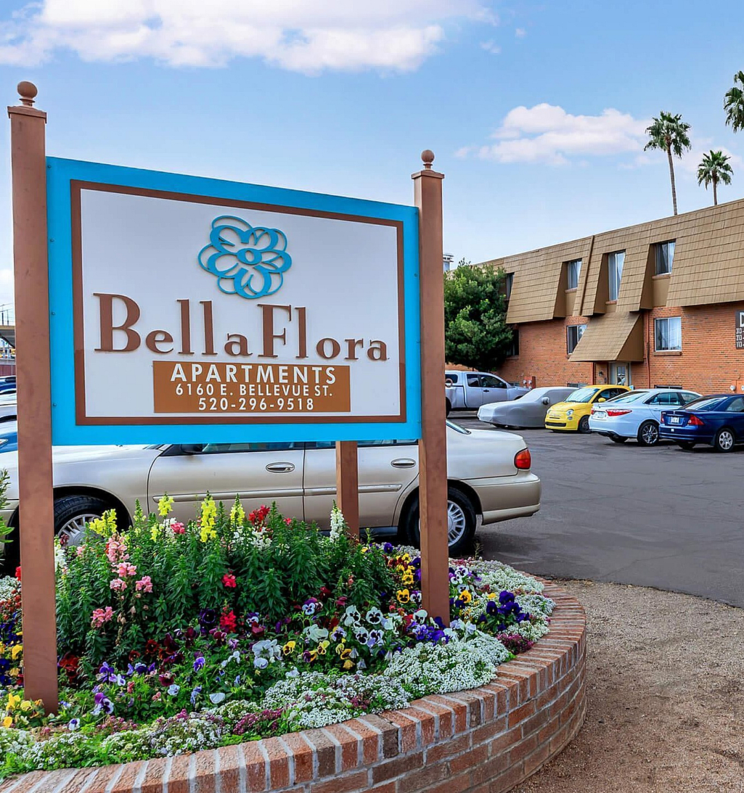 Inviting Bella Flora Apartments with vibrant landscaping, ample parking, and clear accessibility features, set against a clear blue sky.