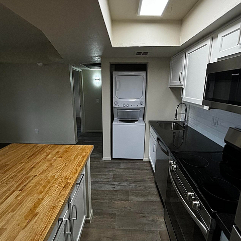 Modern kitchen with sleek black countertops, elegant white cabinetry, central wooden island, and integrated laundry appliances under bright ceiling lights.