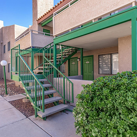 Charming apartment exterior with vibrant green accents and welcoming stairway, surrounded by lush greenery.