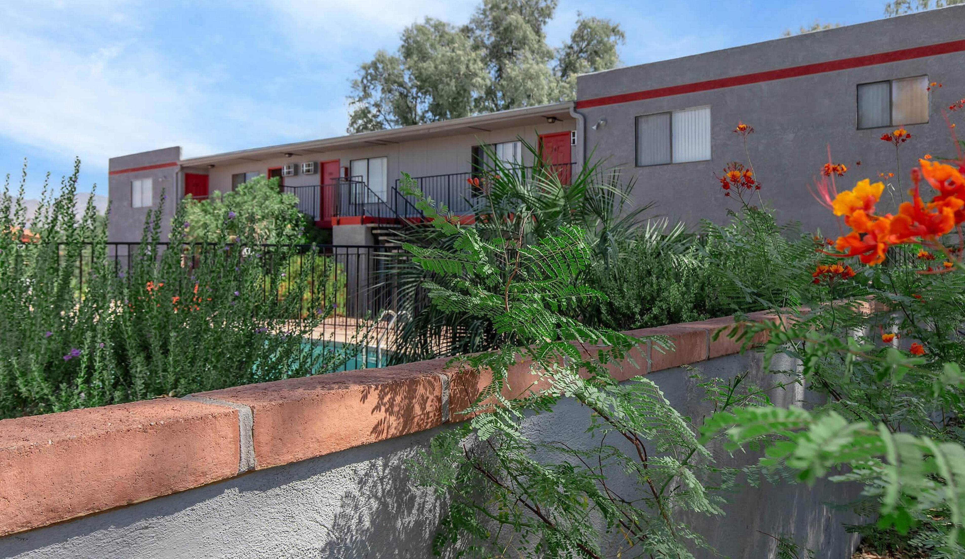 Charming apartment building with vibrant landscaping and inviting balconies, set against a clear blue sky.
