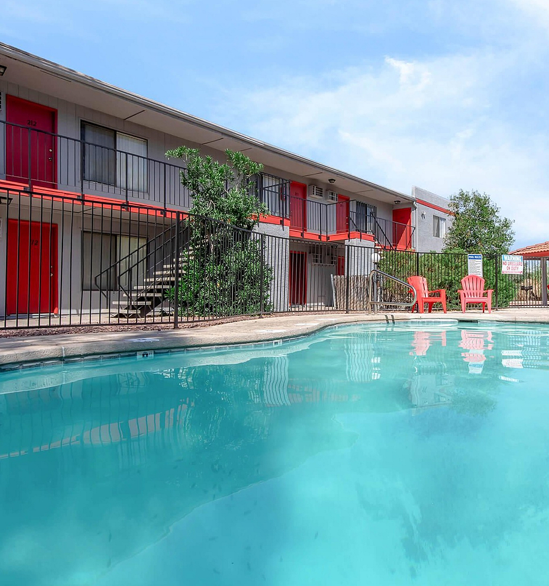 Inviting apartment complex featuring a sparkling pool, vibrant red doors, and charming outdoor seating for relaxation.